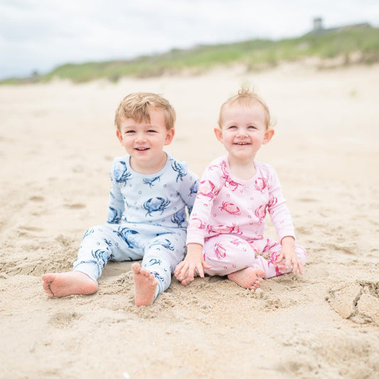 Toddler wearing pink pajamas with cute crab illustrations, standing on a white background, smiling joyfully.