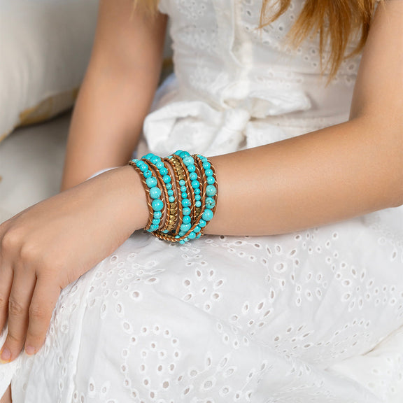 Female hand wearing Ocean Breeze Blue Turquoise Bracelet against a serene ocean backdrop