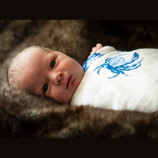 Blue crab-themed baby muslin swaddle blanket and burp cloth set, featuring playful crab illustrations on white fabric.