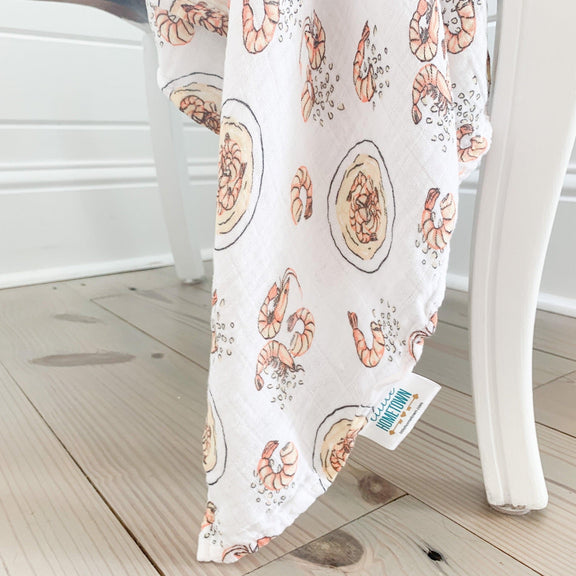 Gift set featuring a shrimp and grits-themed baby muslin swaddle blanket and burp cloth/bib combo.
