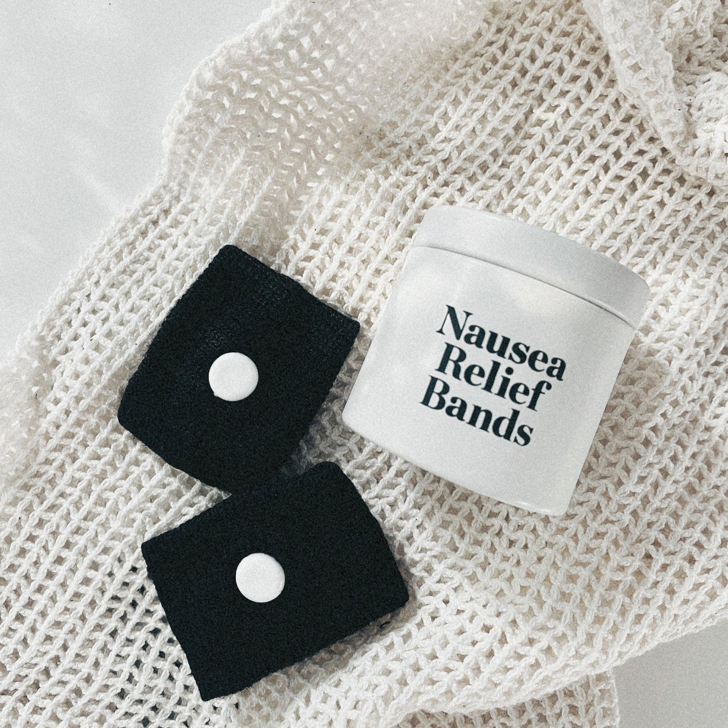 Black nausea bands and a white tin laying on a netted beige bag on a white table.