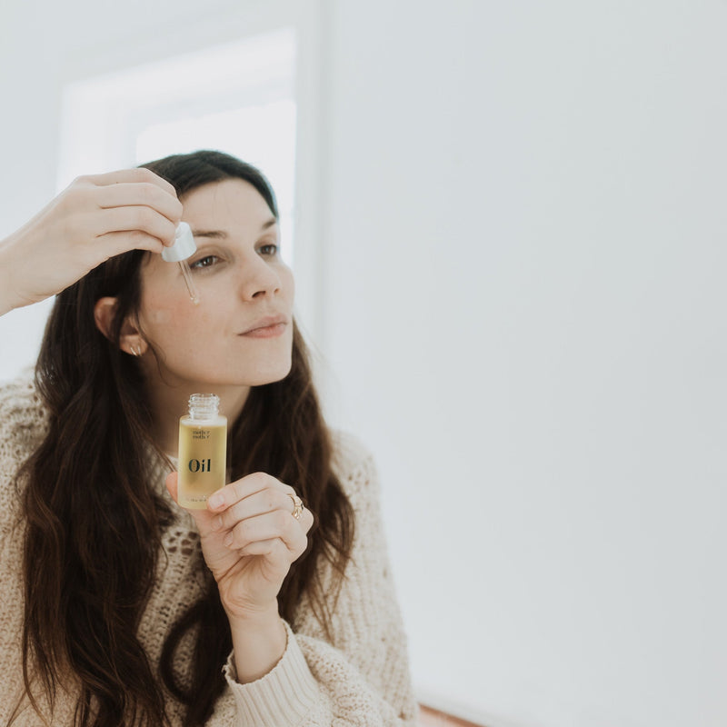 woman with brown hair and beige sweater putting mother mother oil on her face